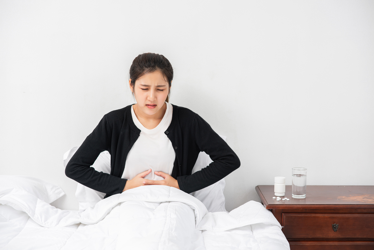 a woman sitting in bed with abdominal pain and pressing her hand