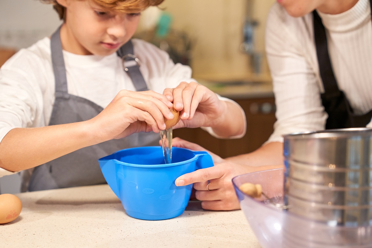 attentive kid cooking with mom and breaking egg for dough