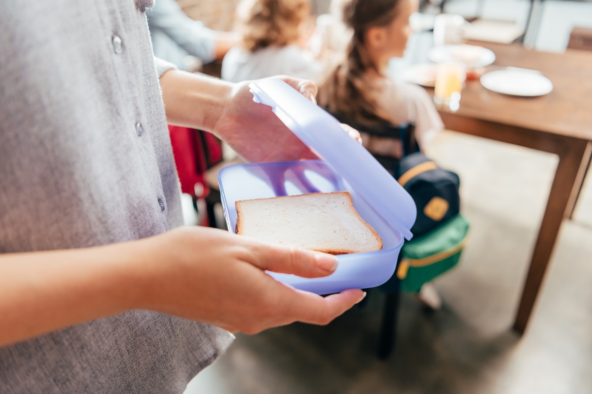 cropped shot of mother packing school lunch in box for children