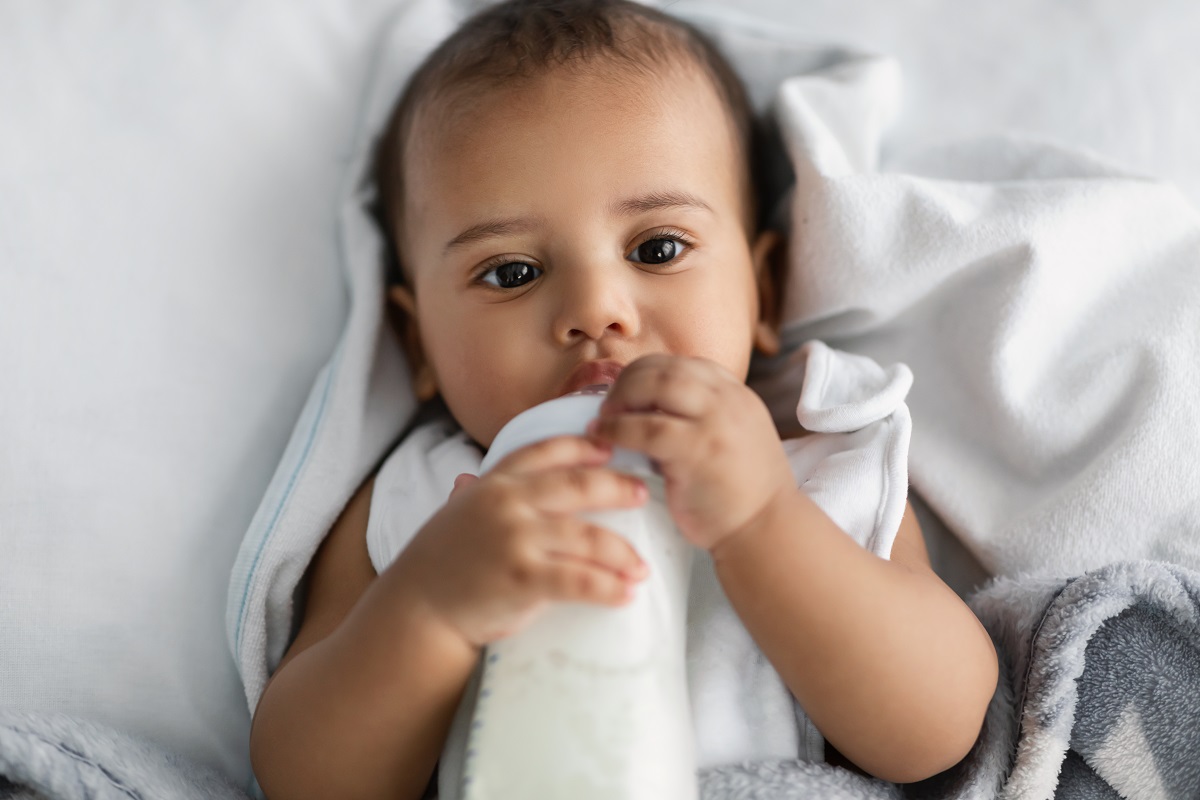 cute little african american child drinking from baby bottle