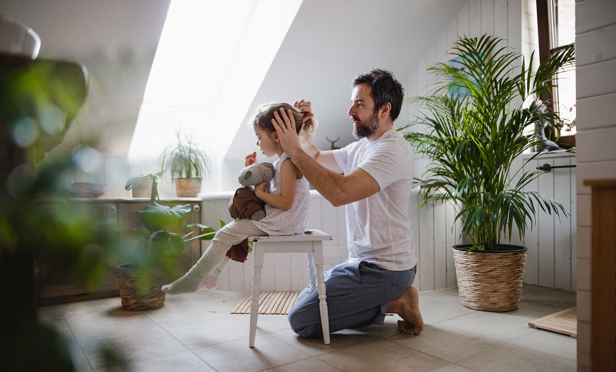 mature father with small daughter indoors in bathroom at home, combing hair.