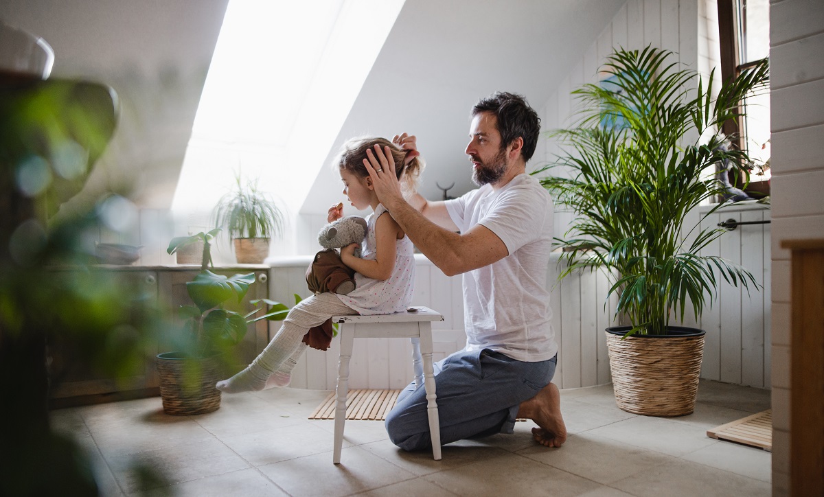 mature father with small daughter indoors in bathroom at home, combing hair.