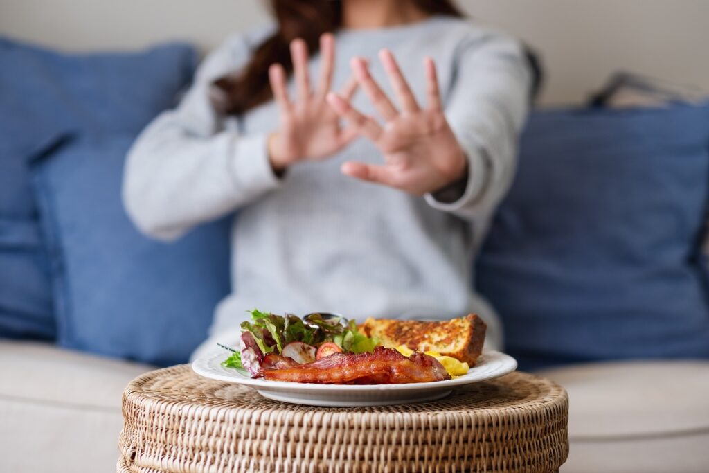 a woman making hand sign to refuse food on the table for dieting