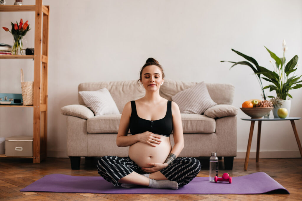 cheerful brunette pregnant woman enjoys music in white wireless headphones and gently touches belly