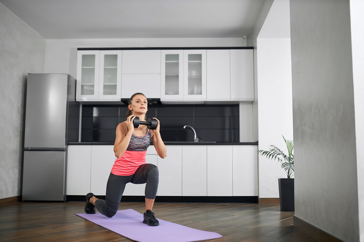 fit young woman practicing lunges at home using dumbbell.