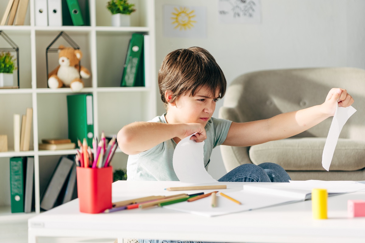 irritated kid with dyslexia punching paper and sitting at table