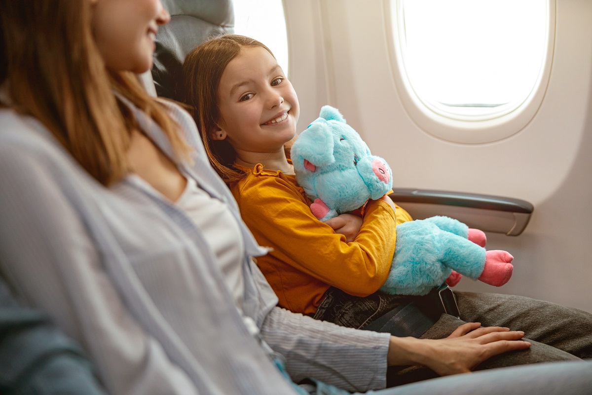 joyful little girl and woman sitting in passenger airplane