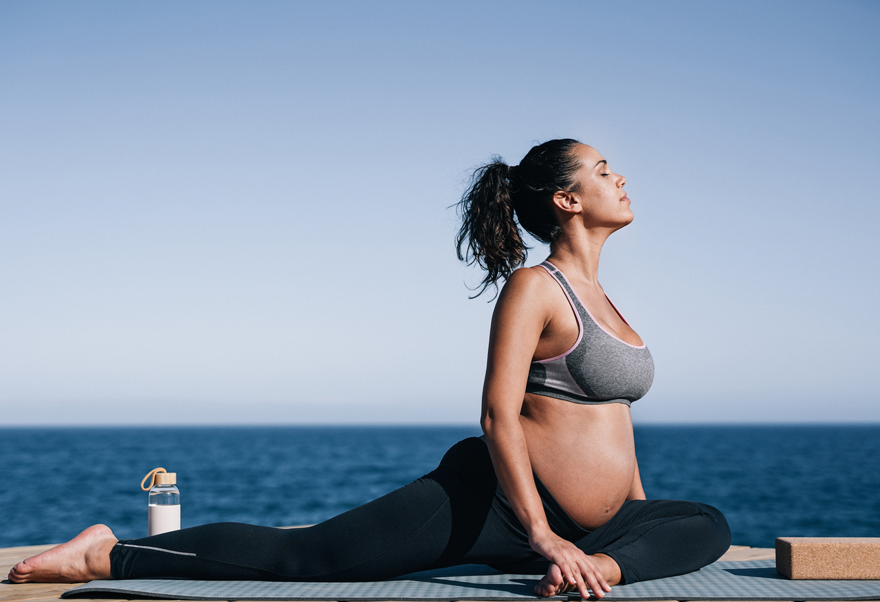 pregnant woman doing yoga exercise routine next to the beach c